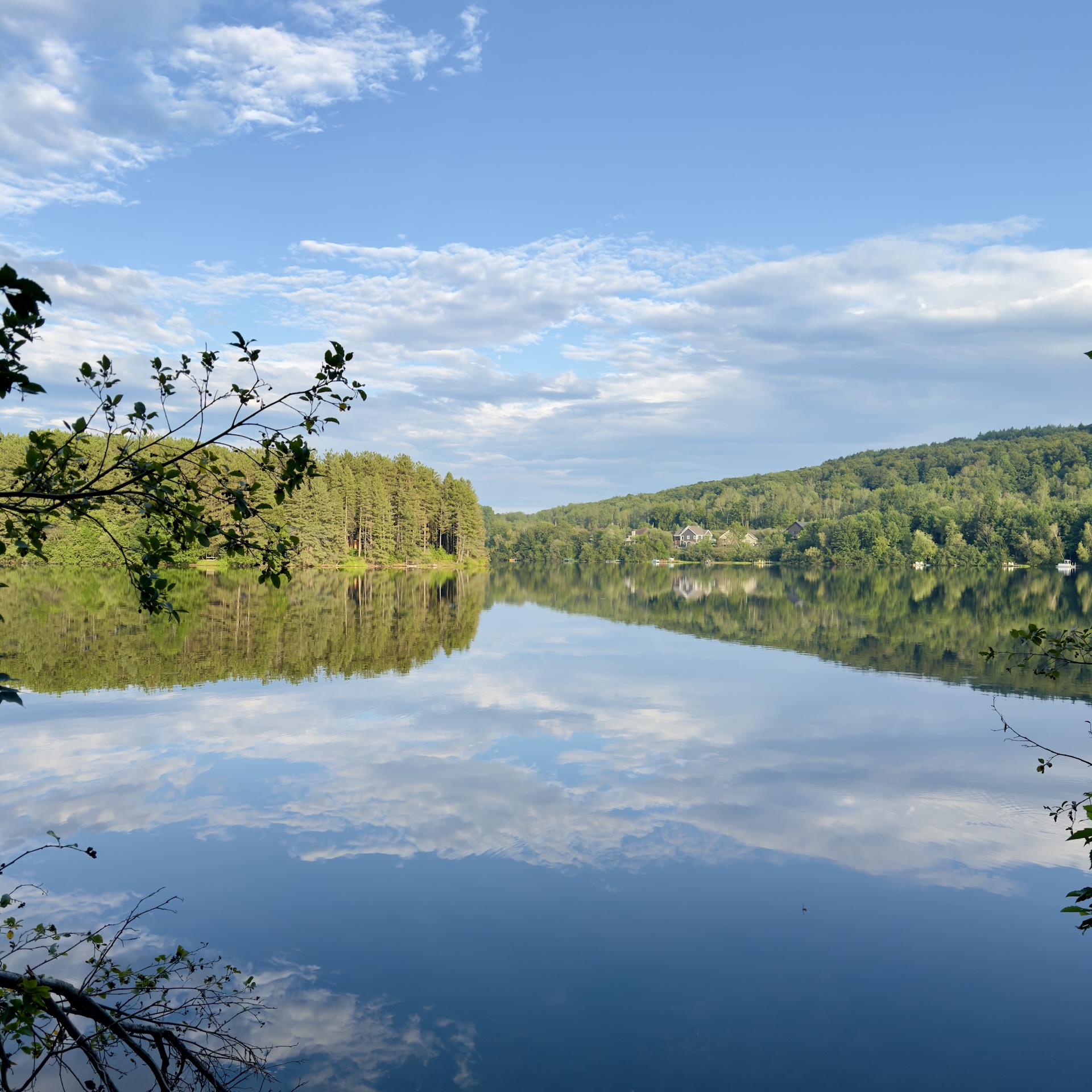 Still lake water reflecting a blue sky, scattered clouds, and green hills, calm after the weather has passed.